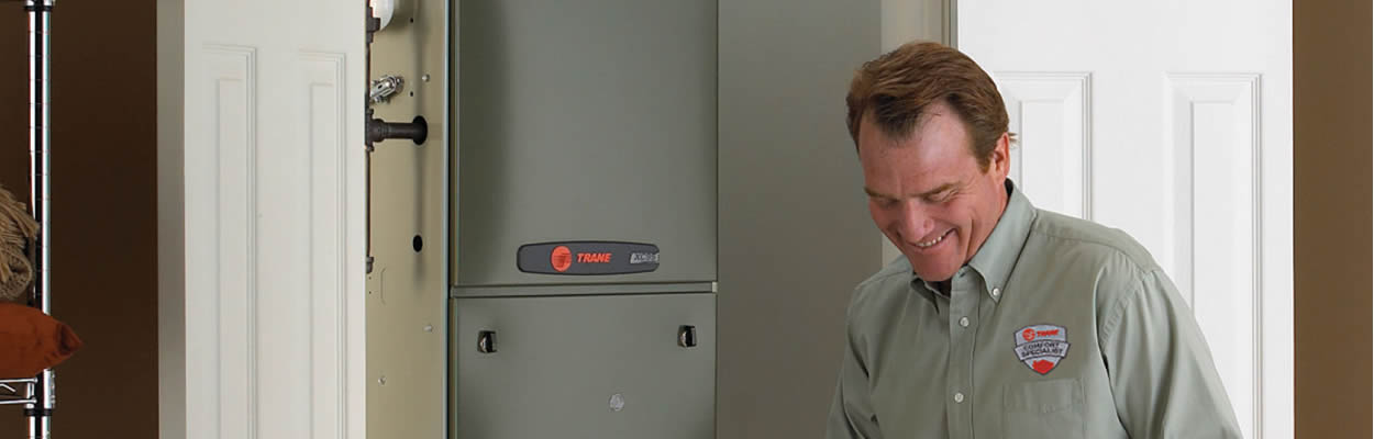 Hvac Technician Standing Next To Trane Furnace Writing On Clipboard (1)